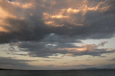 Akşam ları deniz yüzeyinin üzerindeki bulutlu gökyüzüne bakın. Güneş ve bulutların son ışınları ile gün batımından sonra ufuk çizgisi. Hava durumu, mevsim, hava tahmini, kasırga, fırtına.