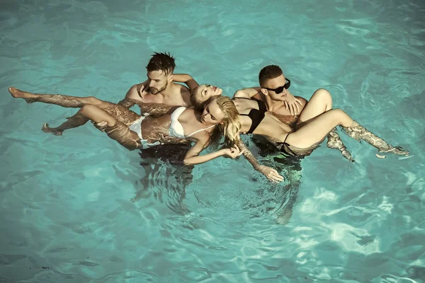 Mannen houden vrouwen in kostuums in blauwe water zwemmen — Stockfoto