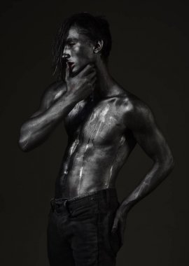 Adam kendine güvenen seksi ifade ile poz dudaklarında parmak tutar. Arzu kavramı. Maço ter çıplak göğsüne akışları ile. Çıplak gövde parıldayan gümüş boya, koyu arka plan ile kaplı olan adam.