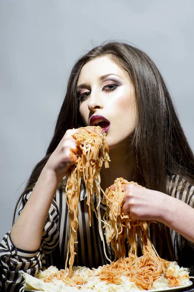 セクシーな女性は 手でスパゲッティを食べる 空腹の少女は イタリア料理の食事を持っています メイクや長いブルネットの髪を持つ美モデルは 夕食を持っています 女性は トマト ケチャップを使ったパスタ料理を食べる ダイエット料理と — ストック写真