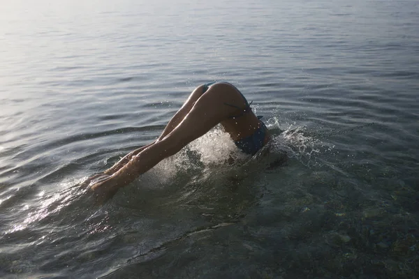 Menina de biquíni saltar para o mar, com salpicos de água. Conceito de mergulho. Mulher sexy magro sob a água do mar, visão traseira. Jovem senhora mergulhou na água, nádegas femininas acima da superfície do mar . — Fotografia de Stock