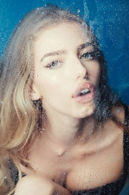 Pencere cam kız yüzü ile yağmur damlaları. Moda ve güzellik. Kız makyaj ile daha önce su ile pencere bırakır. Su ile plastik levha arkasındaki seksi kadın bırakır. Duş ve hijyen kaplıca tedavisi