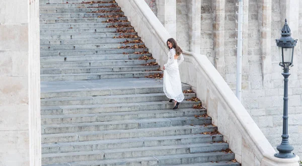 Femme sensuelle sur l'escalier. Femme mariée en robe de mariée blanche, mode. Fille au look glamour. Modèle de mode avec les cheveux longs sur les marches d'escalier. Architecture, structure et design — Photo