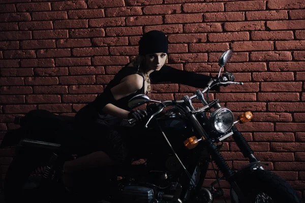 Modelo feminino na motocicleta na escuridão sobre a parede de tijolo — Fotografia de Stock