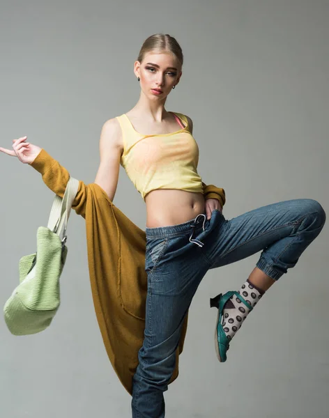 Sporty girl in funny socks jumping with green bag in her hands isolated on gray background