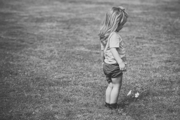 Niño pequeño con el pelo largo y rubio mirando a la flor blanca — Foto de Stock