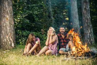 Mutlu arkadaşlar eğlenmeye ormanda piknik. Sakallı adam kız arkadaşı ve kamp ateşi oturan kız kardeşi. Sarışın kız arkadaşı yeme elma ise müzik