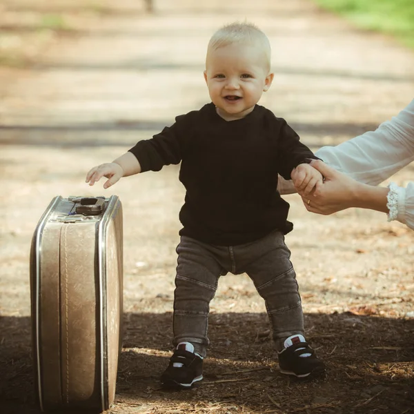 Junge tragen Koffer auf natürliche Landschaft. Junge reisen in den Urlaub mit Retro-Tasche mit Müttern Hand — Stockfoto