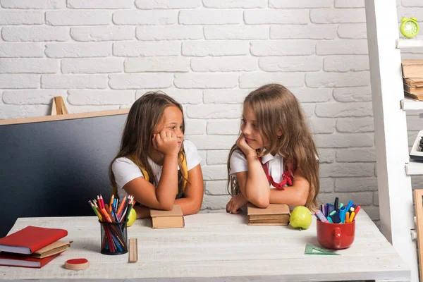 Amistad de las hermanas pequeñas en el aula en el día del conocimiento. Las niñas comen manzana en la hora del almuerzo. niños aburridos de la escuela en la lección en septiembre 1. Hora de la escuela de chicas. Volver a la escuela y a la educación en el hogar — Foto de Stock