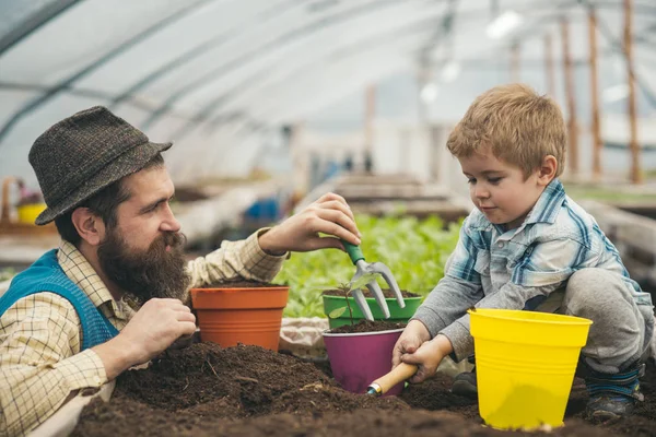 Seitenansicht Papa mit Blick auf seinen netten Jungen, der mit Erde spielt. Hipster mit stylischem Bart und Fedora-Hut hilft seinem Sohn — Stockfoto