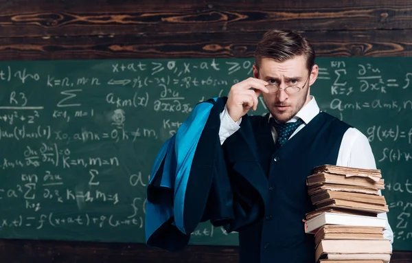 Joven profesor sosteniendo un montón de libros mirando por encima de sus gafas. Aristócrata erudito en la universidad de élite —  Fotos de Stock