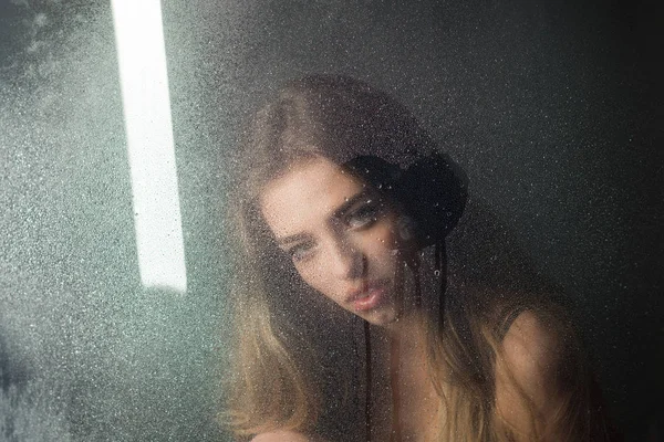 Tratamiento de ducha y spa de higiene. Mujer sexy detrás de la hoja de plástico con gotas de agua. Gotas de lluvia sobre vidrio de ventana en forma de corazón. Ventana con gotas de agua antes de niña con maquillaje. Moda belleza y amor —  Fotos de Stock