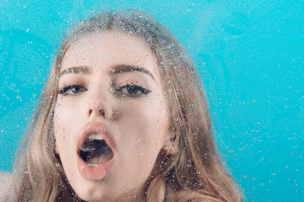 Ventana con gotas de agua antes de niña con maquillaje. Mujer sexy detrás de la hoja de plástico con gotas de agua. Gotas de lluvia en el cristal de la ventana con cara de niña. Tratamiento de ducha y spa de higiene. Moda y belleza —  Fotos de Stock