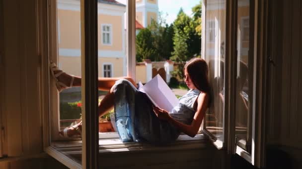 Mladá dívka sedí na okně a snění. — Stock video
