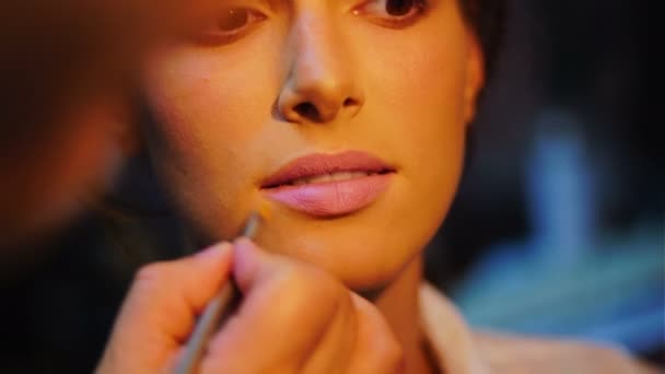メイクアップ アーティストがモデルの唇明るい口紅を適用します。屋内の女の子の化粧を行うメイクアップ アーティスト. — ストック動画