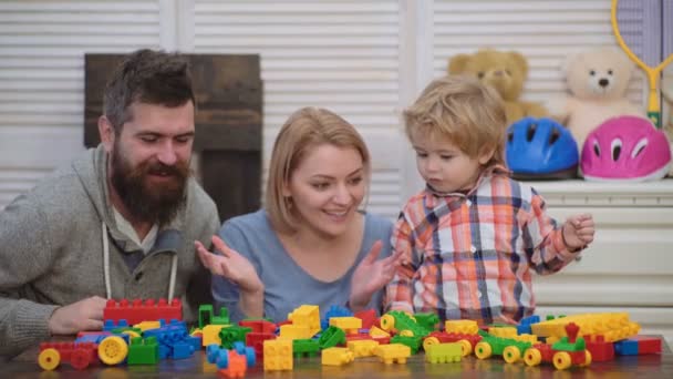 Familia joven en la sala de juegos. Amor concepto familiar. Mamá, papá y niño con juguetes construidos con bloques de plástico. Los padres y el hijo sonriendo, hacer construcciones de ladrillo . — Vídeos de Stock