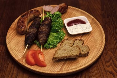 Ahşap şişleri, şiş kebap, ızgara sosis domates ve ekşi krema sosu ile servis et rulo ahşap tahta yuvarlak. Restoran yemek kavramı. Marul ve ekmek yemek iştah açıcı dekore edilmiş.