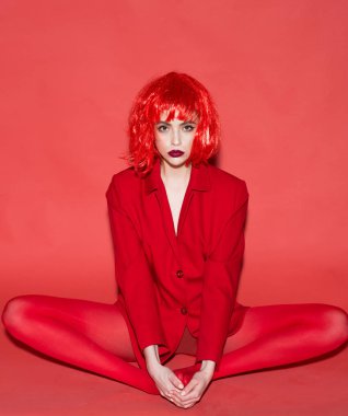 Yoga kavramı. Karanlık bayanla kameraya bakarak dudakları ve lotus poz oturur. Makyaj ve kırmızı peruk toplam kırmızı kıyafetiyle poz olan kadın. Kız kırmızı resmi ceket, kırmızı arka planda gizemli yüz.