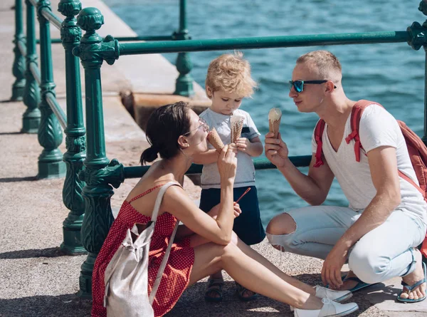 Mother and father with son eat ice cream at sea. Summer vacation of happy family. Child with father and mother. Family travel with kid on mothers or fathers day. Love and trust as family values.