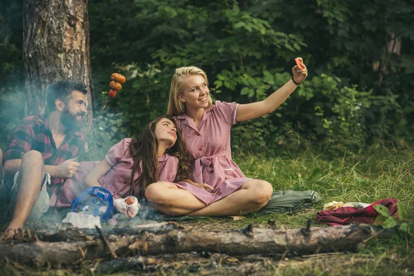 Menina loira tomando selfie na floresta. Amigos sorridentes posando com salsichas. Jovens acampando na floresta — Fotografia de Stock