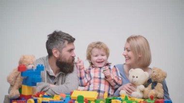 Genç aile inşaat plastik blokları ile oyun oynamak. Aile Oyunları kavramı. Anne ve çocuk mutlu yüzler ile kırmızı tuğla tutun. Baba, anne ve oğlu ışık ahşap arka plan üzerinde oyun odası.