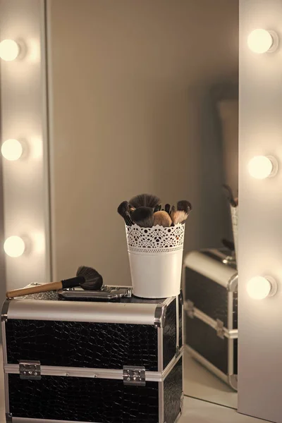 Makeup case with brushes at mirror on dressing table. Professional make up kit in beauty salon. Visage course, cosmetics, make up. Makeup artist tools and kit in dressing room.