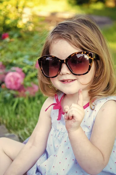 Dziewczyna uśmiecha się z podniesionym palcem w letnim ogrodzie — Zdjęcie stockowe