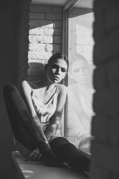 Mujer con cara de pensar sentarse solo en el alféizar de la ventana en el interior —  Fotos de Stock