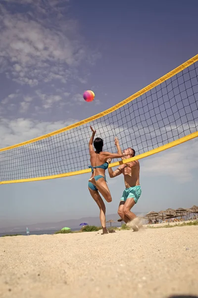 Woman and man fit, strong, healthy, doing sport on beach. Beach volleyball concept. Couple have fun playing volleyball. Young sporty active couple beat off volley ball, play game.