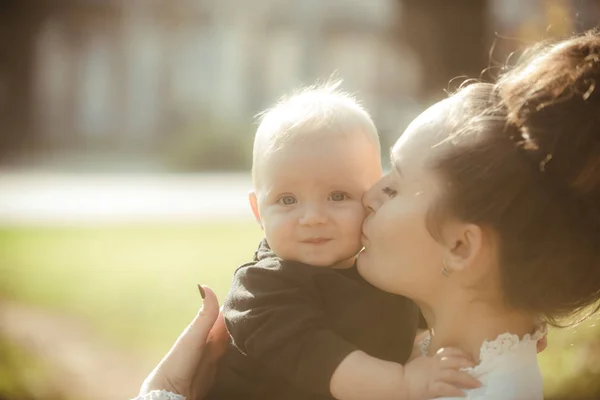 Una mujer besa al niño con amor. Madre e hijo pequeño. Mamá y bebé al aire libre. Concepto del día de las madres. Feliz familia disfruta de un día soleado. Amor cuidado y confianza — Foto de Stock