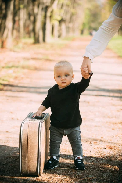 Reisendes Kind trägt Koffer auf Naturlandschaft. Junge reist mit Vintage-Tasche mit der Hand der Mutter — Stockfoto