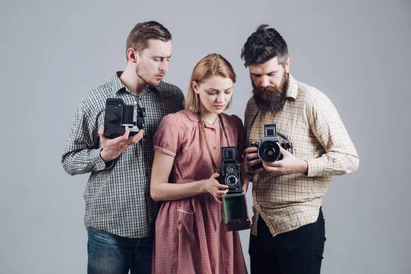 Men, woman on interested faces looks at camera on grey background. Company of busy photographers with old cameras, filming, working. Men in checkered clothes, retro style. Vintage photography concept.