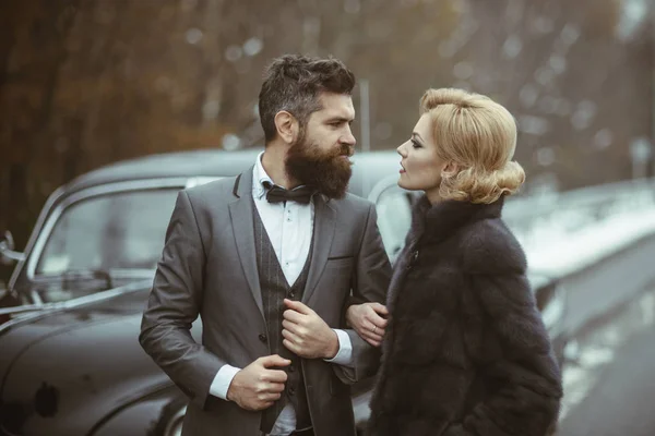 Casal apaixonado no encontro romântico. Homem barbudo e mulher sexy em casaco de peles. Retro coleta de carro e reparação de automóveis por motorista mecânico. Viagem e viagem de negócios ou engate caminhadas. Escolta de menina por segurança . — Fotografia de Stock