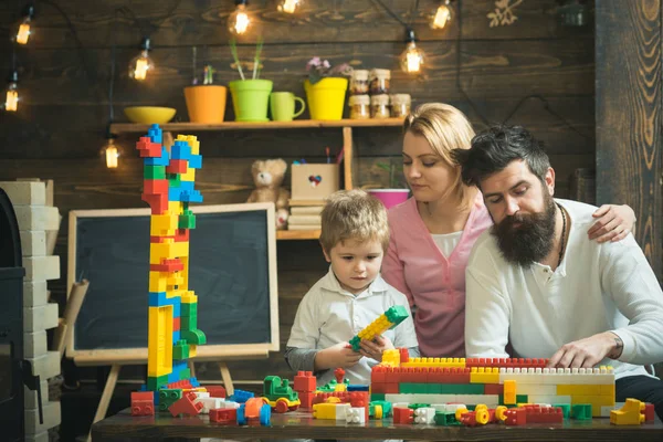 Concepto de ocio familiar. Los padres abrazos, ver jugar al hijo, disfrutar de la paternidad. Niño con los padres juegan con bloques de plástico, construir la construcción. Padre, madre e hijo lindo jugar con ladrillos constructor . — Foto de Stock