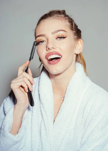 Girl on smiling face wears bathrobe, grey background. Lady play with sharp blade of straight razor. Barber concept. Woman with attractive lips holds straight razor in hand. — Stock Photo, Image