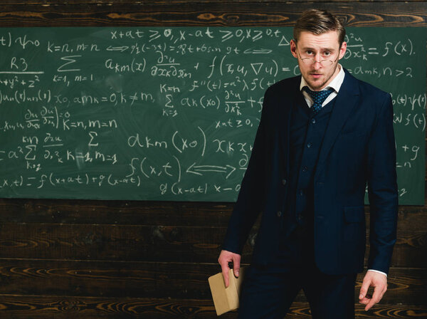 Intelligent man in suit and glasses holding book. Tired young teacher talking to audience