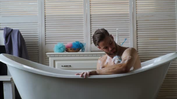 Joven hombre guapo relajándose en la bañera. Un hombre con barba bañándose en una bañera blanca. Hombres cubiertos de espuma baño de burbujas en bañera de lujo con felicidad y relax . — Vídeo de stock