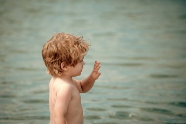 Deniz kıyısı el sallayarak şirin çocuk. Çocuk ciddi bir yüz ile deniz suyu dur. Elveda ve ayrılık kavramı. Yaz tatili ile tatil veda üzerinde yürümeye başlayan çocuk. Yaz aylarında üzüntü