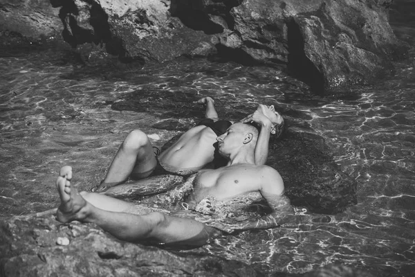 Man och kvinna ligga i havet mellan reven på solig sommardag. Par på semester har simning. Par i kärlek lägger i vattnet nära sten eller rock på bakgrund. Semester och smekmånad koncept — Stockfoto