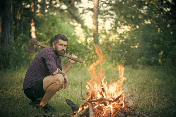 Uomo boscaiolo con ascia guarda fiamma falò — Foto Stock