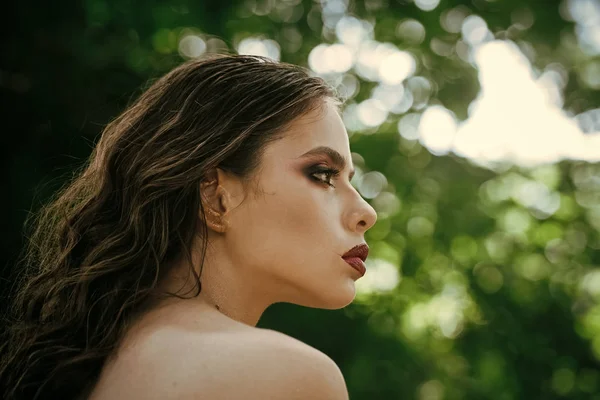 Fille avec le visage de maquillage, beauté. Femme avec de longs cheveux bruns sur la nature. Femme avec coiffure bouclée et épaule nue le jour d'été. Modèle de mode avec look glamour. Soins capillaires, thérapie et traitement — Photo