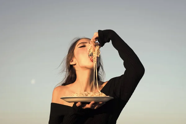Junge schöne Frau isst Spaghetti, auf blauem Himmel Hintergrund. — Stockfoto