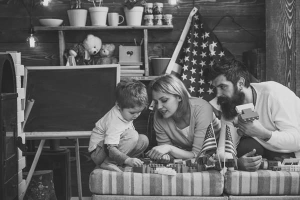 Família americana feliz brincando com construtor em casa. mãe e pai ajudando a construir a construção com tijolos. playroom com americano, EUA bandeira no fundo — Fotografia de Stock