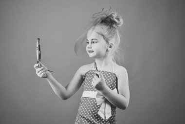 Küçük kız ruj ve ayna tutun. Moda ve güzellik, pinup stil, çocukluk. Makyaj retro görünüm ve Kuaför. Şık elbise, makyaj kız çocuk. Kozmetik, güzellik ile Retro kız moda