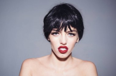 Siyah peruk Bayan gri arka plan üzerinde olun. Kız çıplak omuz ile poz sakin dalgın yüzünde. Makyaj ve visage kavramı. Çekici dudaklar kadınla kameraya benziyor.