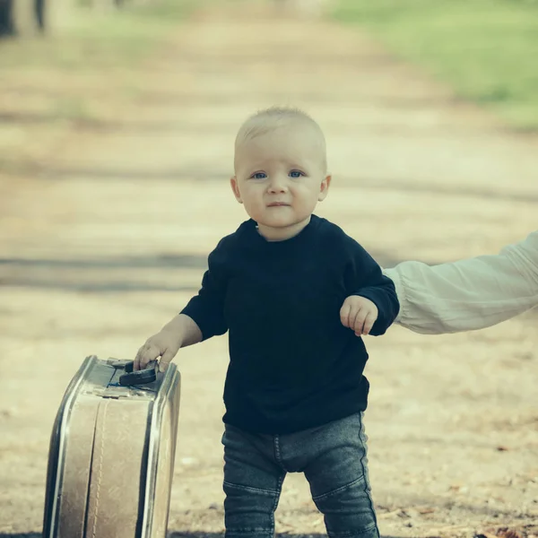 Μικρό αγόρι μεταφέρει ρετρό βαλίτσα στο φυσικό τοπίο. Παιδί που ταξιδεύουν για διακοπές με την τσάντα με το χέρι μητέρες. Παιδί ταξιδιώτη με υπαίθριο χώρο φύλαξης αποσκευών. Διακοπές ταξίδια και περιπλάνησης — Φωτογραφία Αρχείου