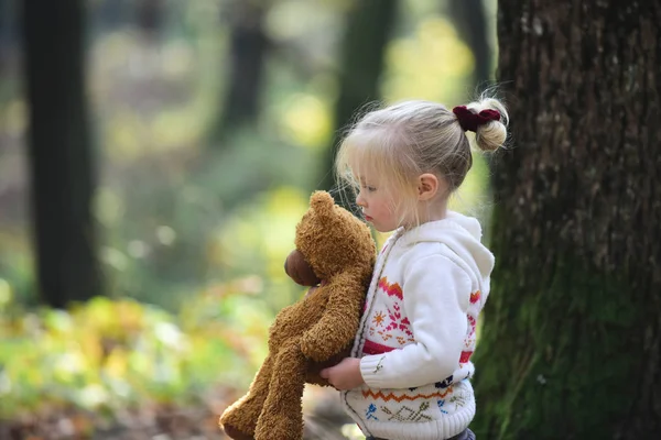 Klein kind lopen weg met teddy beer met herfst bladeren en zonlicht schijnt op achtergrond — Stockfoto