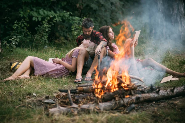 Jovem casal apaixonado desfrutando de fim de semana romântico na natureza. Homem barbudo a olhar para a namorada loura com admiração. Grupo de amigos fazendo piquenique na floresta — Fotografia de Stock