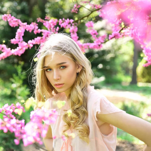 Mädchen mit verträumtem Gesicht, zarte Blondine neben violetten Blüten des Judasbaums, Naturhintergrund. Frühjahrsblüher Konzept. Dame spaziert an sonnigem Frühlingstag im Park. junge Frau genießt Blumen im Garten, defokussiert. — Stockfoto