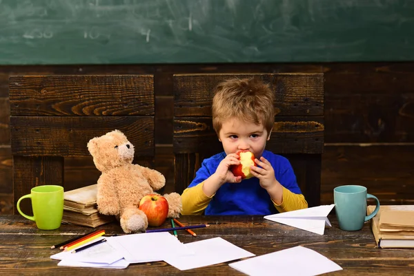Przerwie od szkoły. Gryzienie apple w klasie głodne dziecko. Mały chłopiec bawi się papierowy samolot i Miś — Zdjęcie stockowe